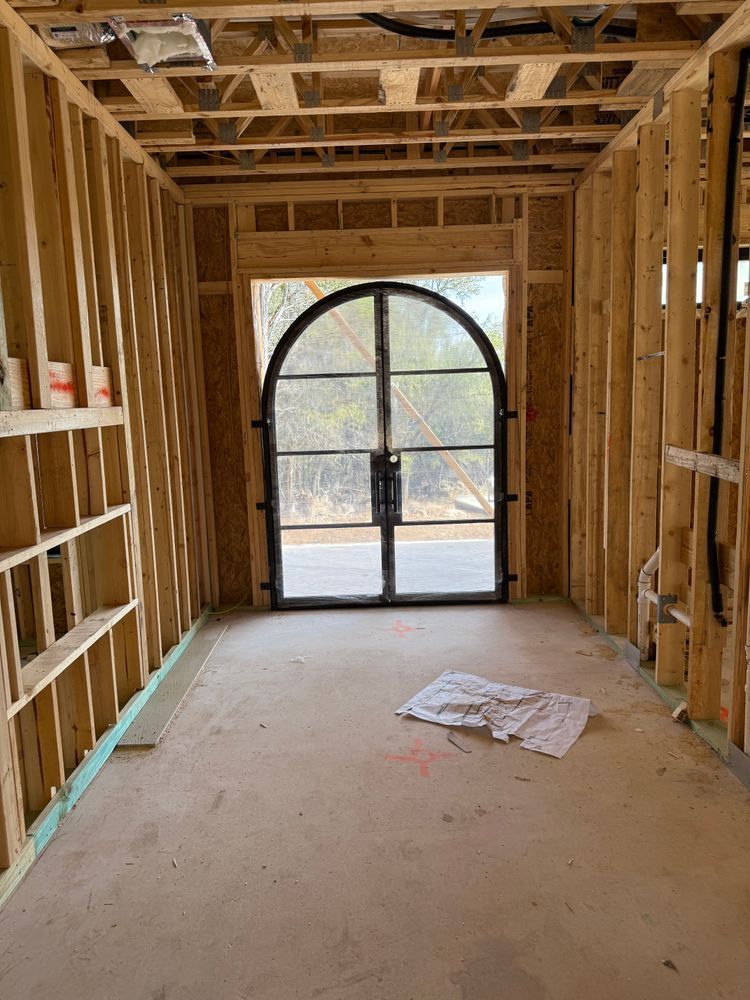 Unfinished interior hallway framed with wood studs, leading to a glass arched door at the end.