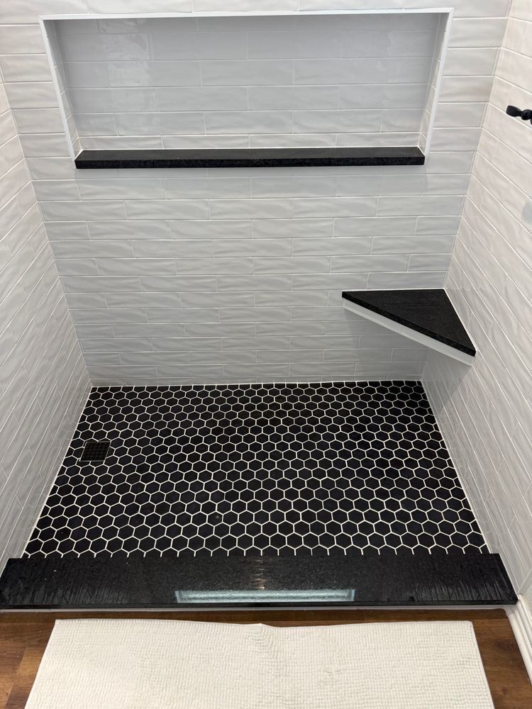 Empty white tiled shower with black hexagon floor and built-in corner shelf.