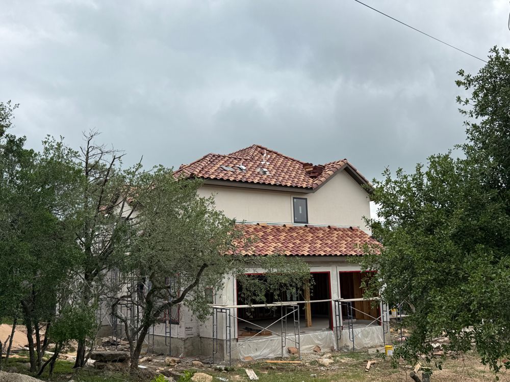 Rural house with red-tiled roof, porch, and trees under a cloudy sky
