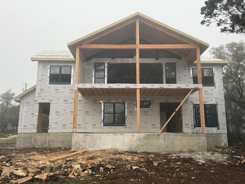 Partially built two-story house with exposed framing and stone exterior on a muddy construction site