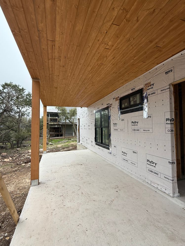 Covered porch with wooden ceiling, concrete floor, and unfinished exterior wall with windows and house wrap