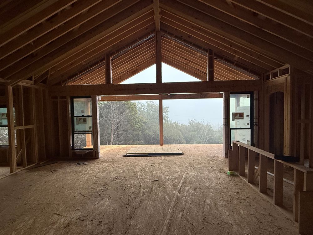 Empty unfinished attic with exposed wooden beams and large windows overlooking trees