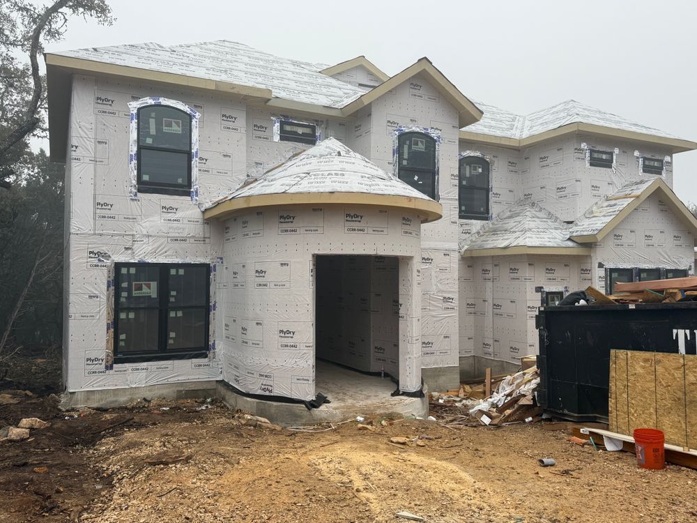Two-story house under construction with white exterior, unfinished yard, and a dumpster nearby
