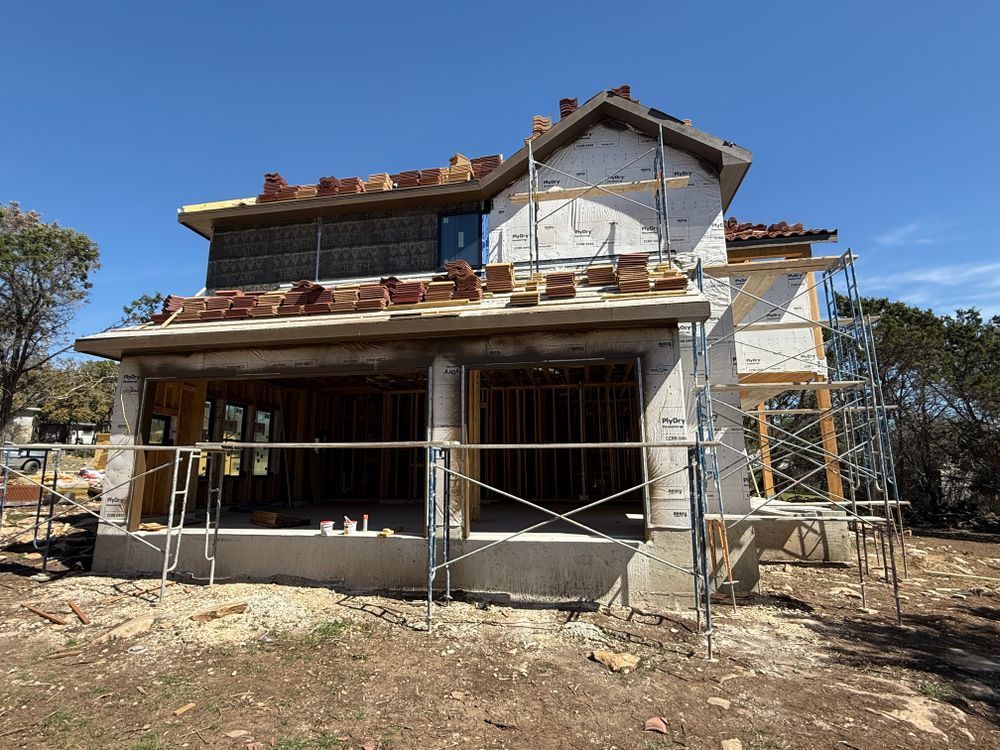 Two-story house under construction with scaffolding and a partially finished roof under a clear blue sky