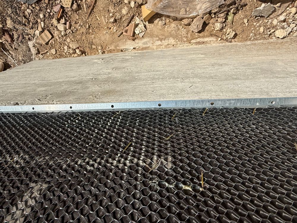 Black mesh mat against a concrete curb with rocky dirt in the background