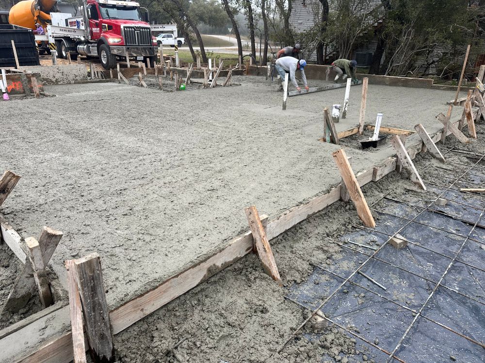 Fresh concrete slab being poured and leveled at a construction site with workers and a cement truck