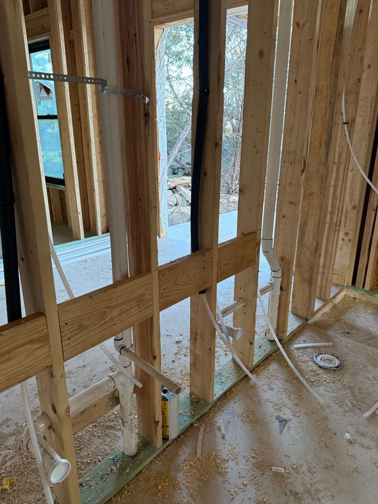 Unfinished wood-framed room with studs, window opening, and exposed wiring on a plywood floor.