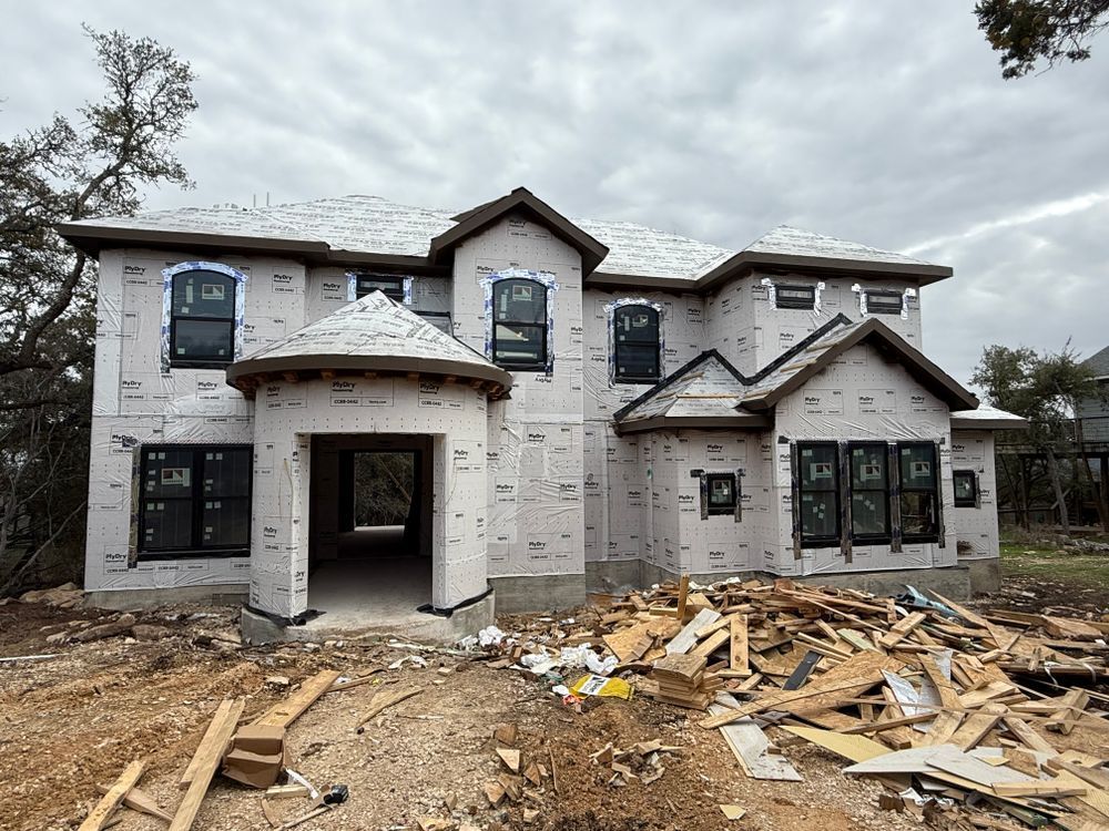 Partially built two-story house with white siding, dark windows, and construction debris in the front yard