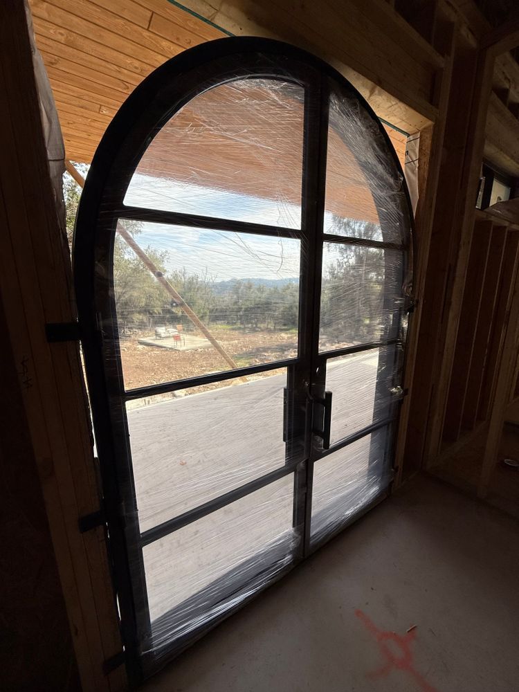 Arched screened door with black metal frame, looking out onto a dusty outdoor landscape.