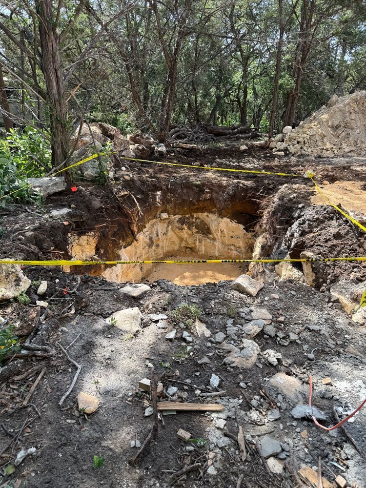 Rope-marked excavation pit in a wooded area with exposed soil and debris around it