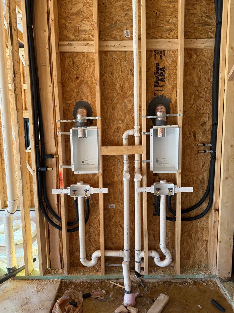 Two utility boxes with exposed white pipes and black cables installed on unfinished wood wall framing