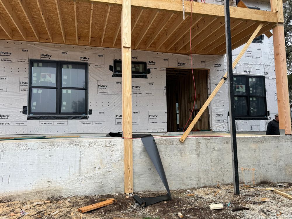Partially built house with porch scaffolding, black-framed windows, and a door under construction