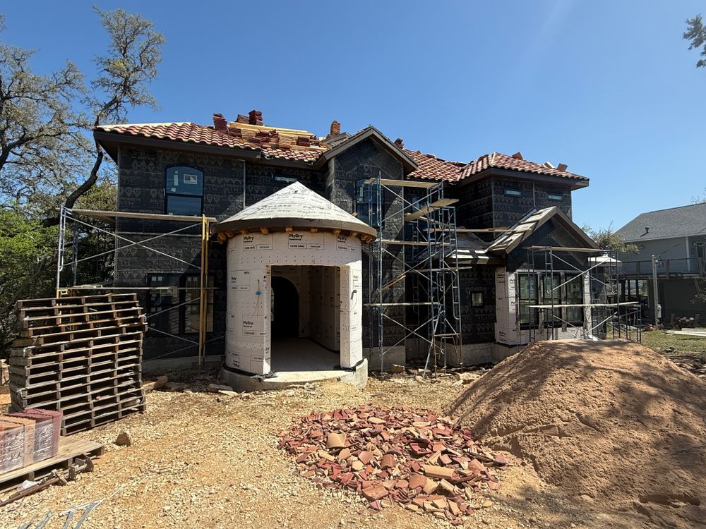 House under construction with scaffolding, exposed brick, and a dirt foreground under a clear blue sky