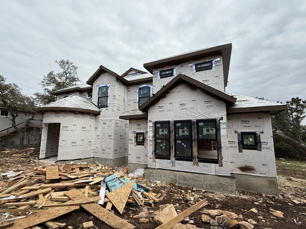Partially built white house with exposed wood framing and debris in front, under cloudy sky