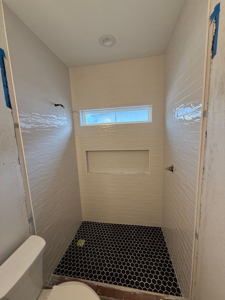 Empty shower with black hex tile floor, white walls, and a small frosted window above a recessed shelf.