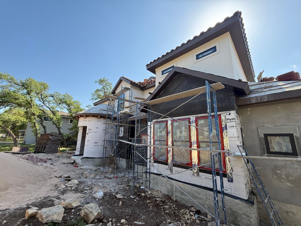 House under construction with scaffolding and stone exterior in a sunny yard