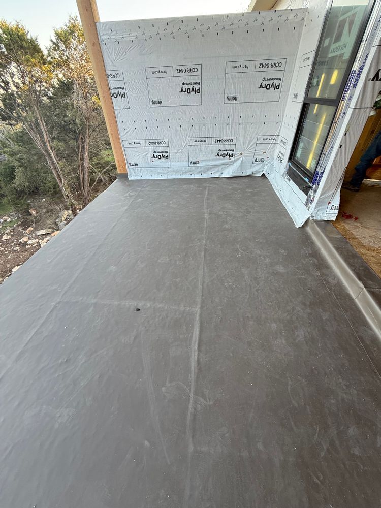 Partially built porch with gray flooring and wrapped exterior walls beside trees