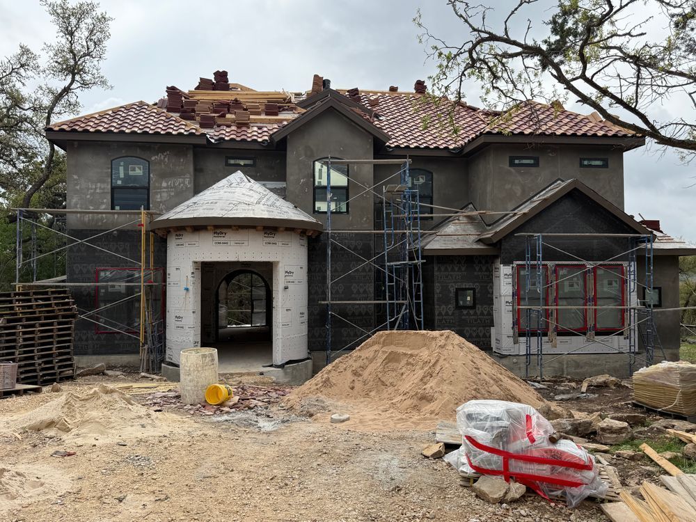 Two-story house under construction with scaffolding, exposed roof, and piles of dirt in the front yard