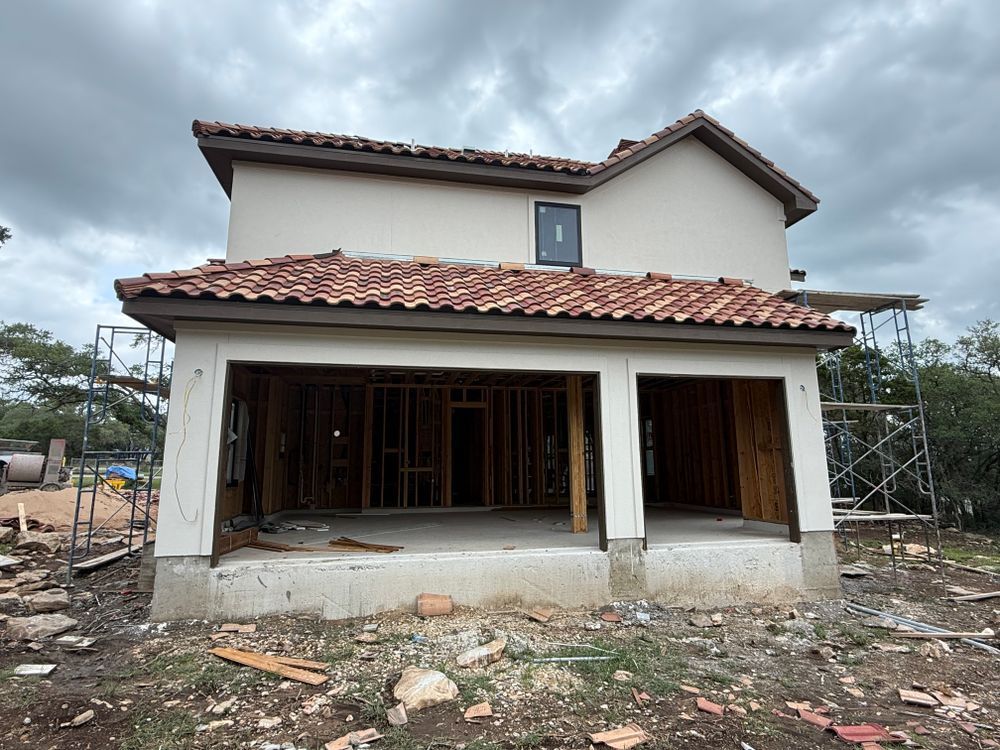 Partially constructed two-story house with white walls, terracotta roof, and open front porch under overcast sky
