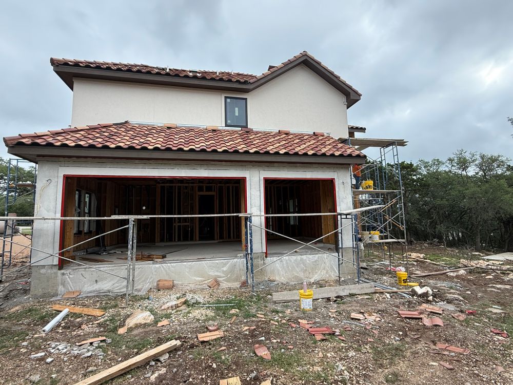 Two-story house under construction with tiled roof, unfinished front porch, and scattered building debris.