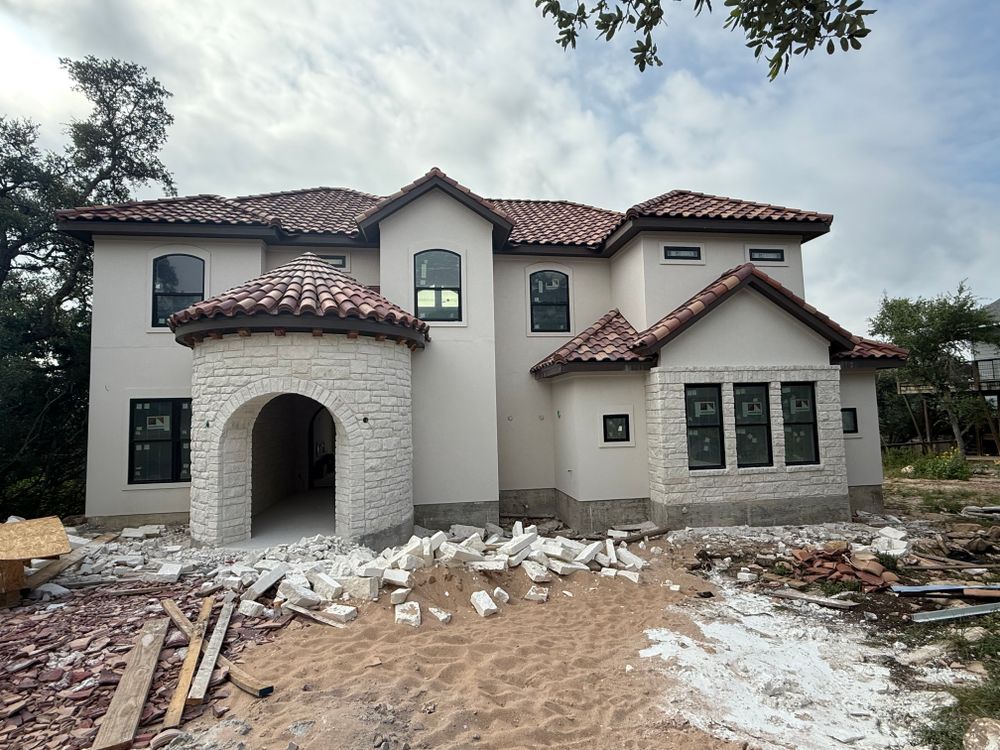 Partially built two-story stucco house with red tile roof and construction debris in front
