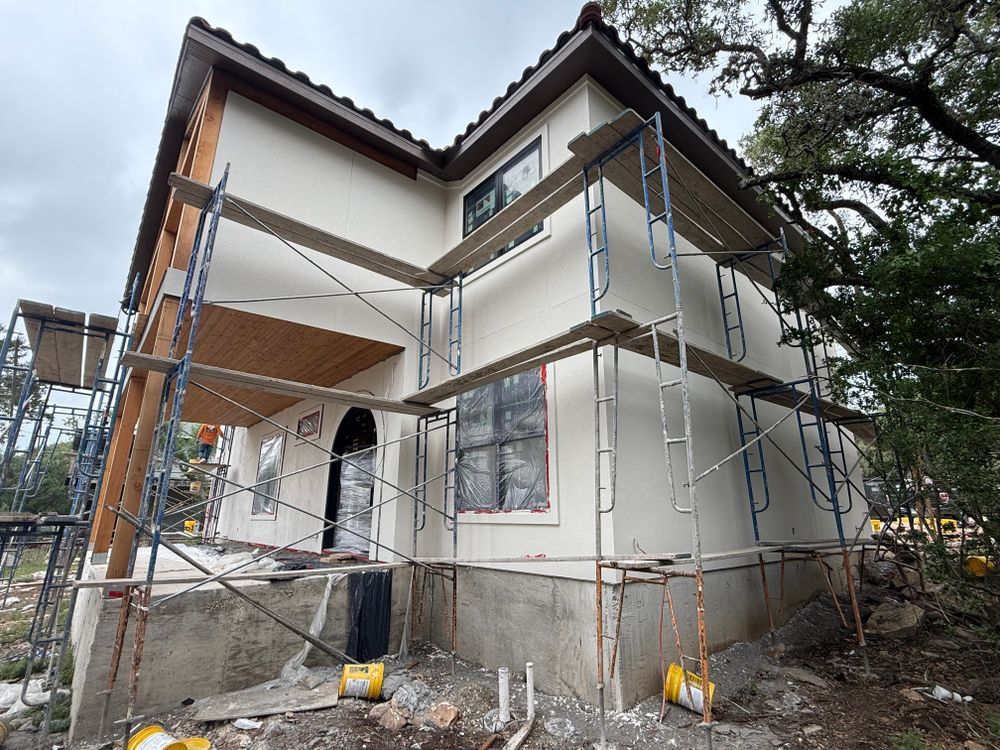 Two-story house under construction with metal scaffolding and a covered porch area.