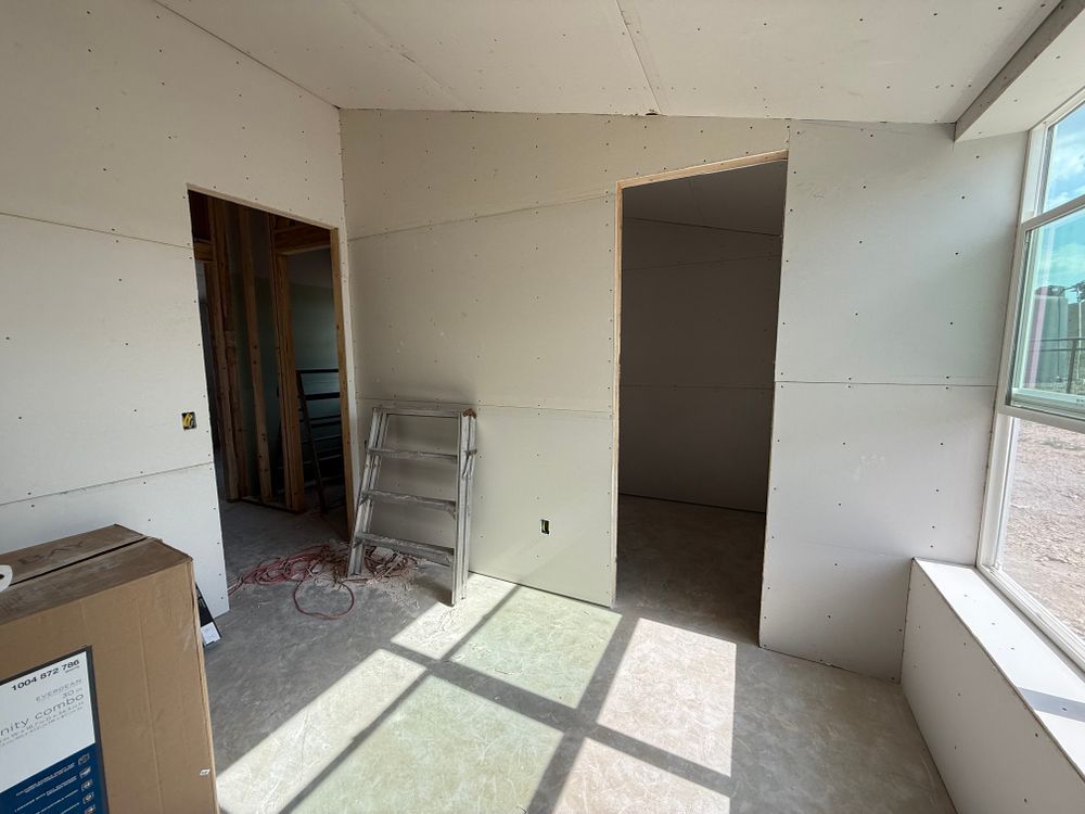 Empty room under renovation with unfinished drywall, ladder, and sunlight on the floor