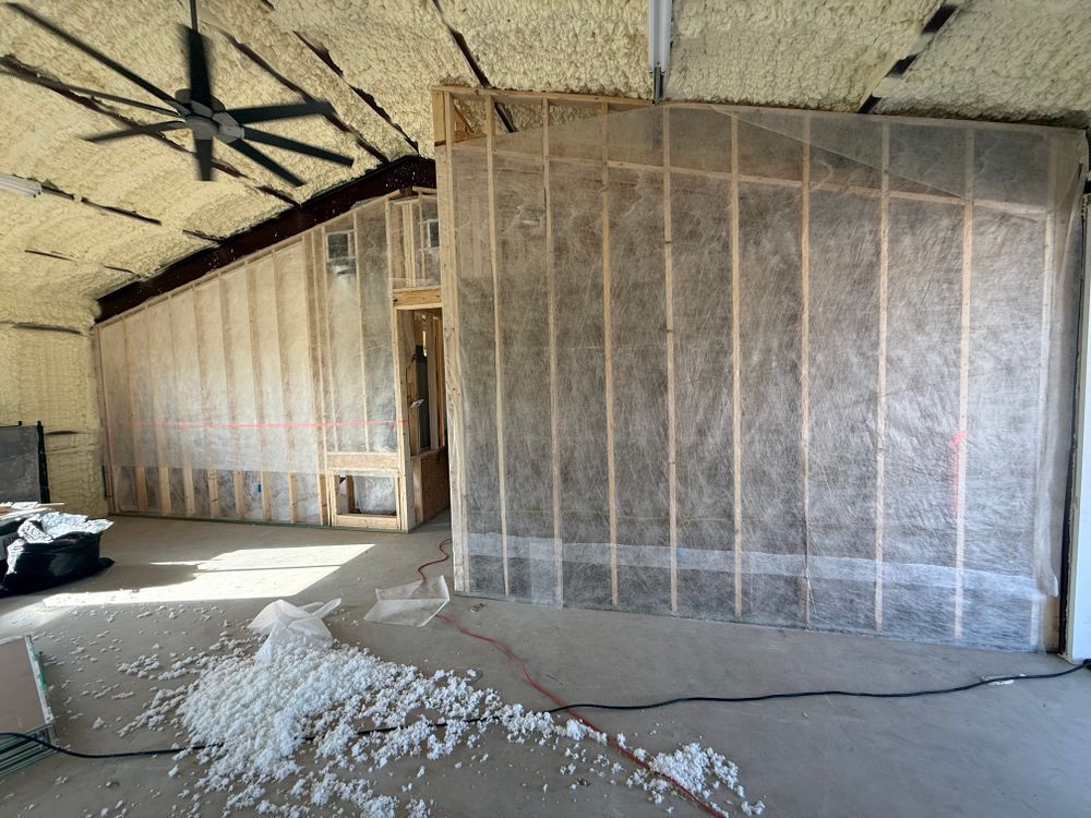 Unfinished room with exposed insulation walls, sloped ceiling, debris on floor, and a window opening.