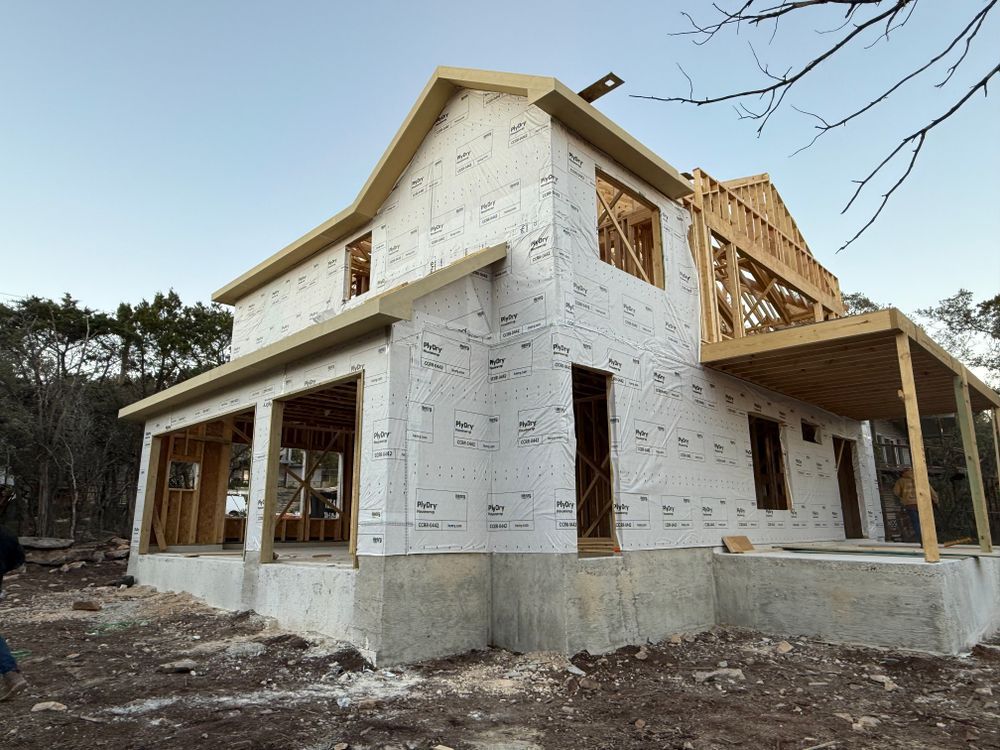 Partially built two-story house wrapped in white house wrap, with exposed wooden framing and a front porch