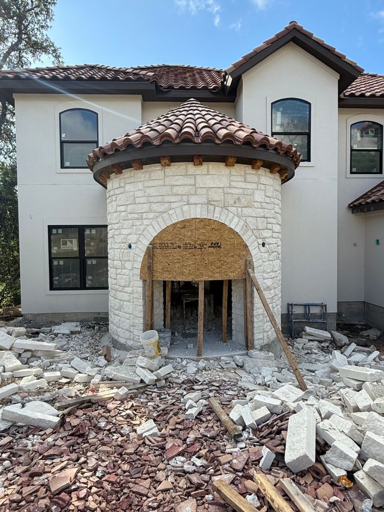 Partially built stucco house with stone entrance and construction debris scattered in front