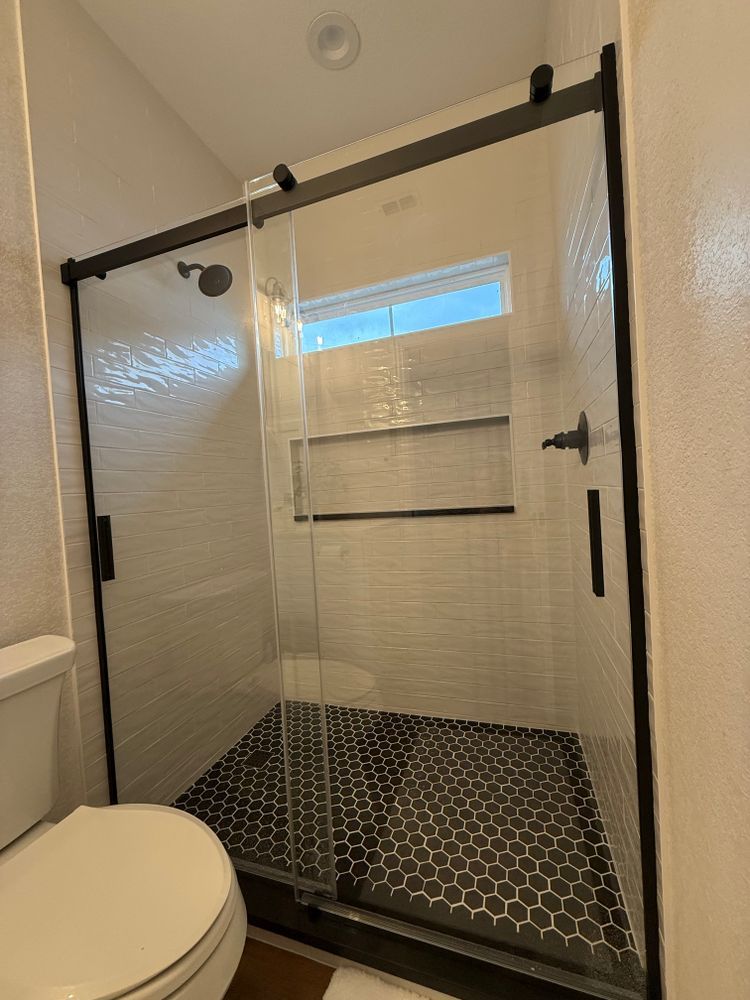 Bathroom shower with glass doors, black hardware, white tile walls, and hexagon floor tile.