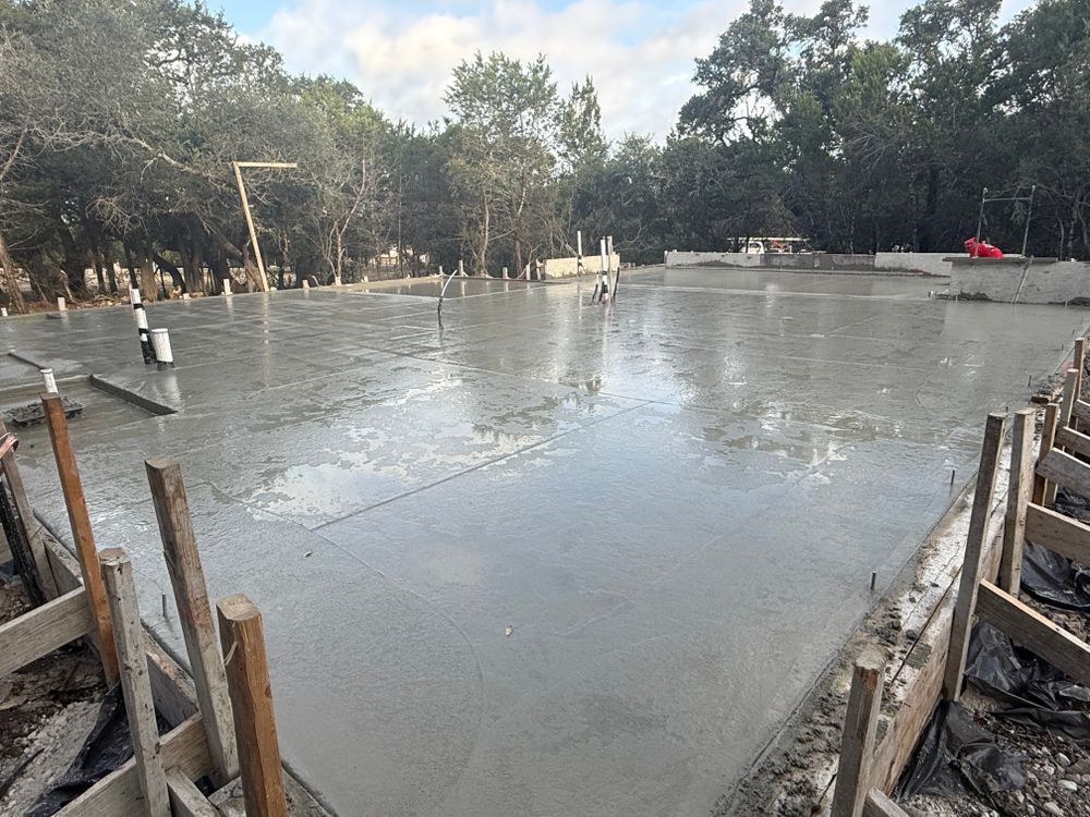 Wet concrete slab being poured at an outdoor construction site, with trees in the background.