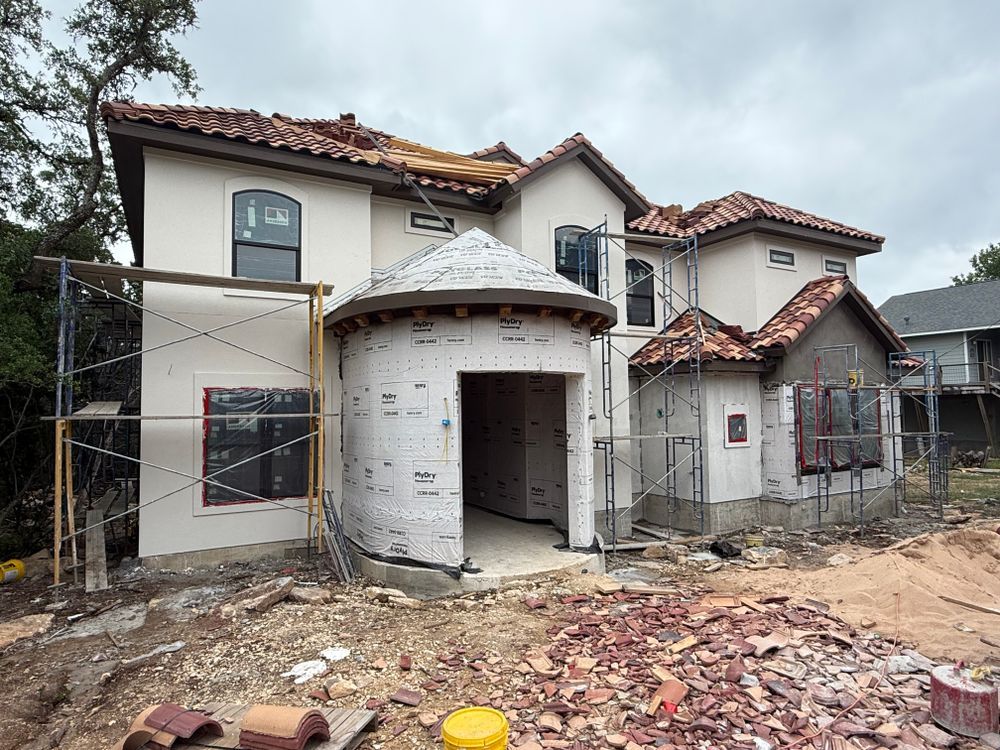 Partially built two-story house with white stucco walls, red tile roof, and exposed construction materials