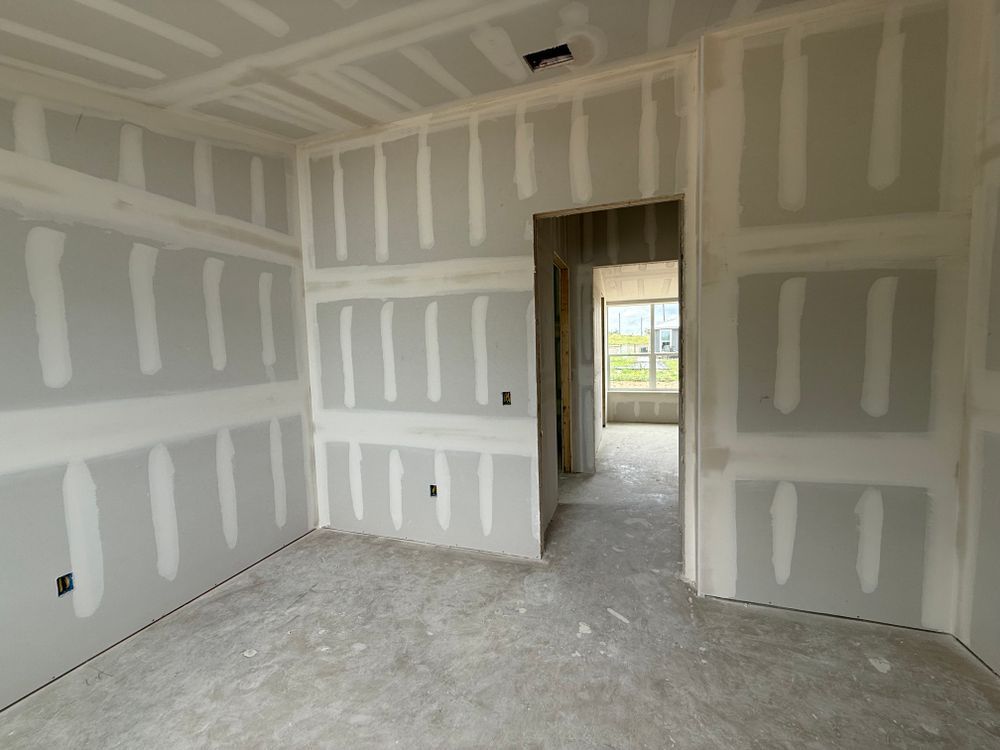Unfinished drywall room with doorway to a bright hall and window beyond.