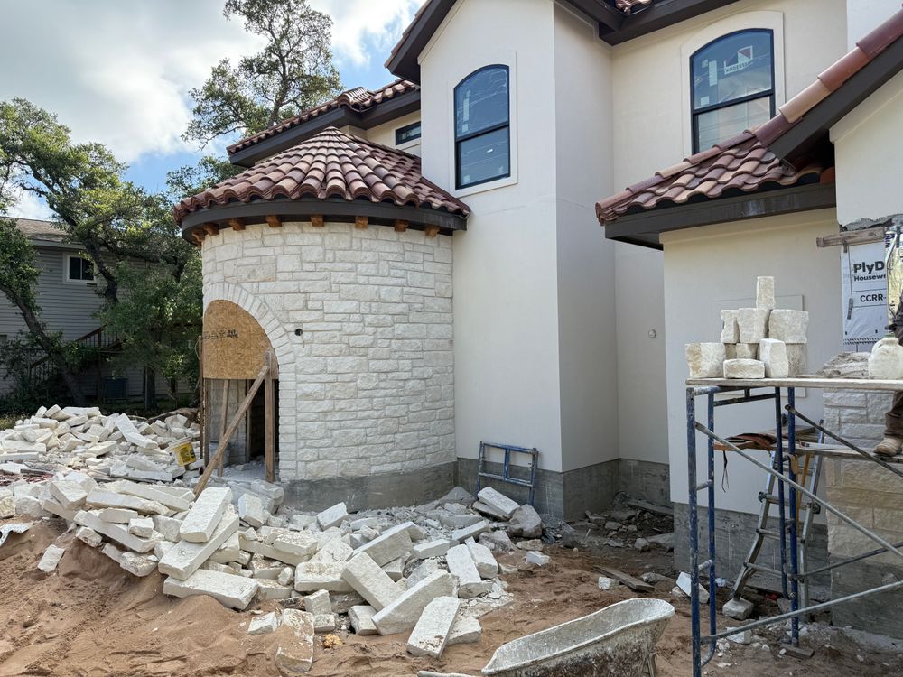Stone house under construction with rubble on the ground and a scaffold beside the wall