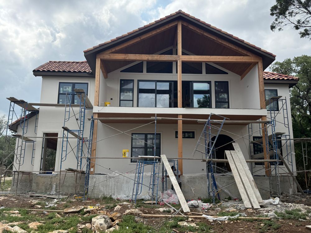 Front of a two-story house under construction with scaffolding, exposed wood framing, and debris in the yard