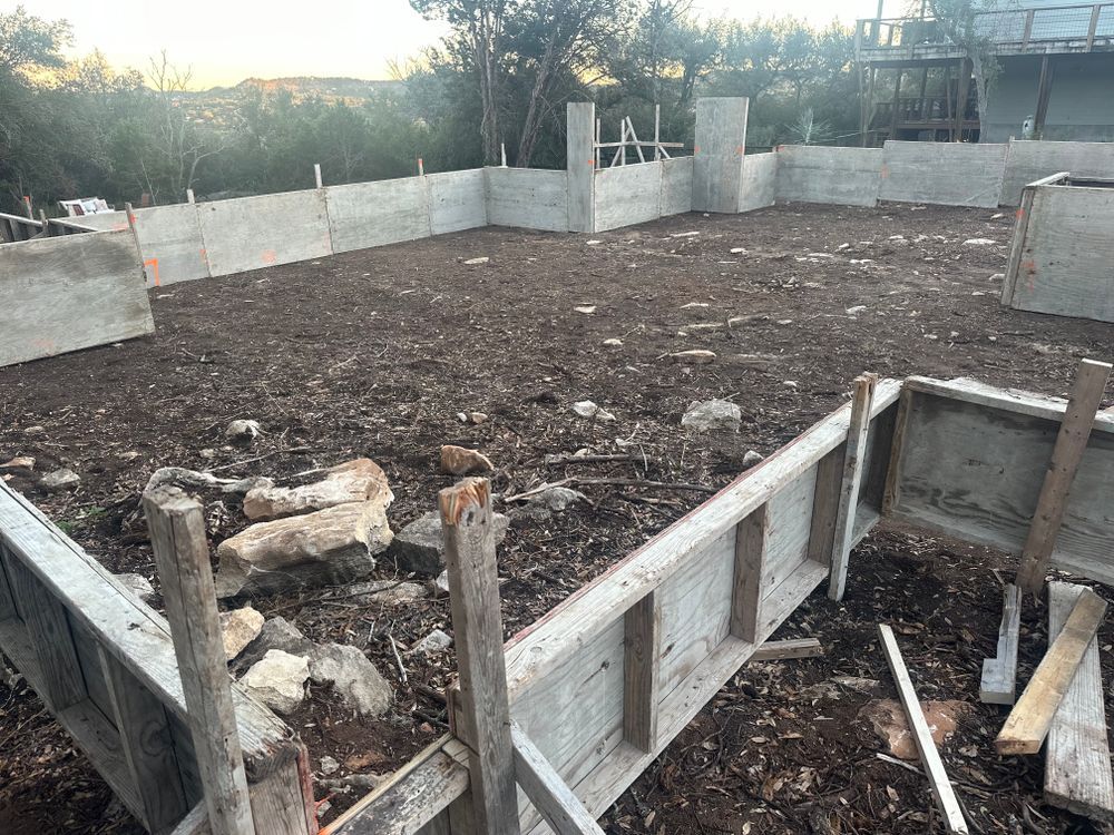 Concrete foundation under construction with rebar, formwork, and a dirt lot inside a low block wall