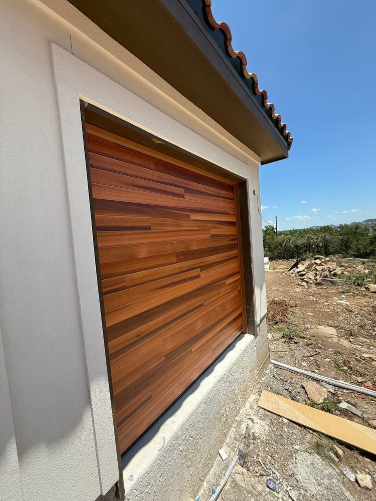 Exterior wall with a wooden window shutter on a stucco house, beside a rocky lot under a clear sky