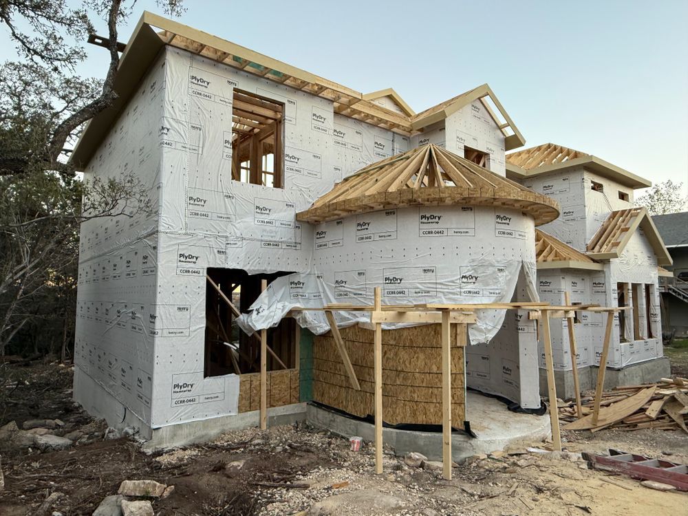 Partially built two-story house wrapped in white sheathing, with roof framing and scaffolding in front