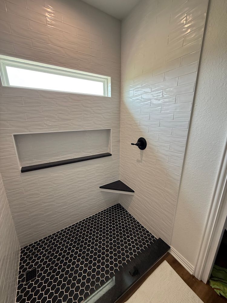 White-tiled shower with black hex floor, built-in niche, window, and matte black fixtures