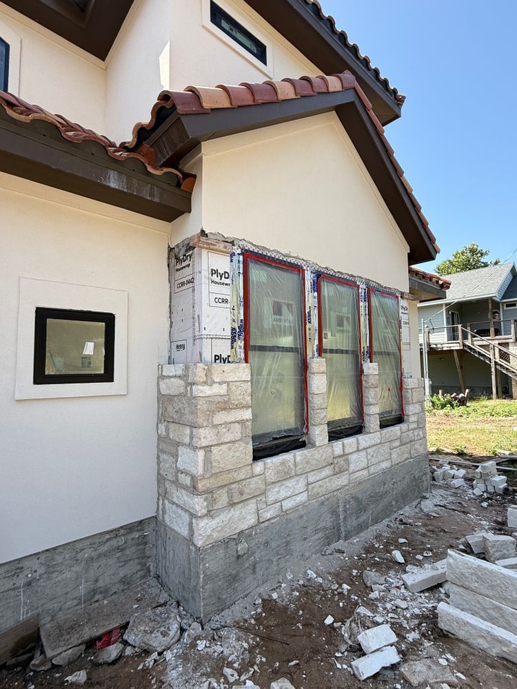 House exterior with newly framed windows and stone trim, surrounded by construction debris under a clear sky