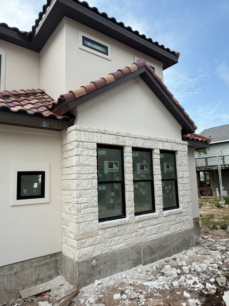 Exterior of a house with stone-clad bay windows, white walls, and a red-tiled roof under construction
