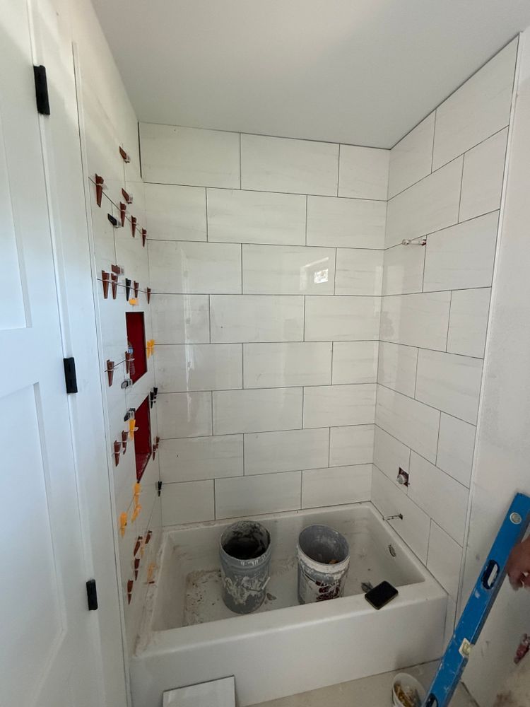Small bathroom under renovation with white tiled walls, a tub, and exposed plumbing fixtures.