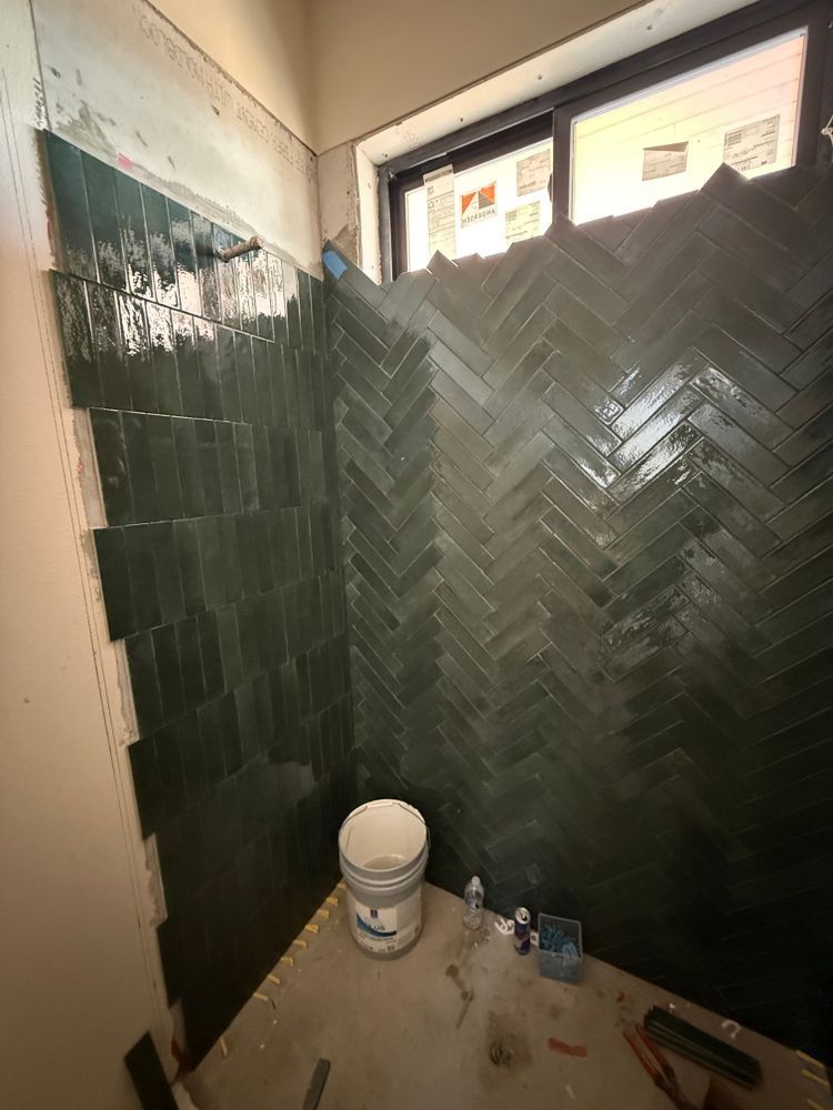 Partially tiled bathroom under renovation with dark green herringbone walls and a paint bucket on the floor