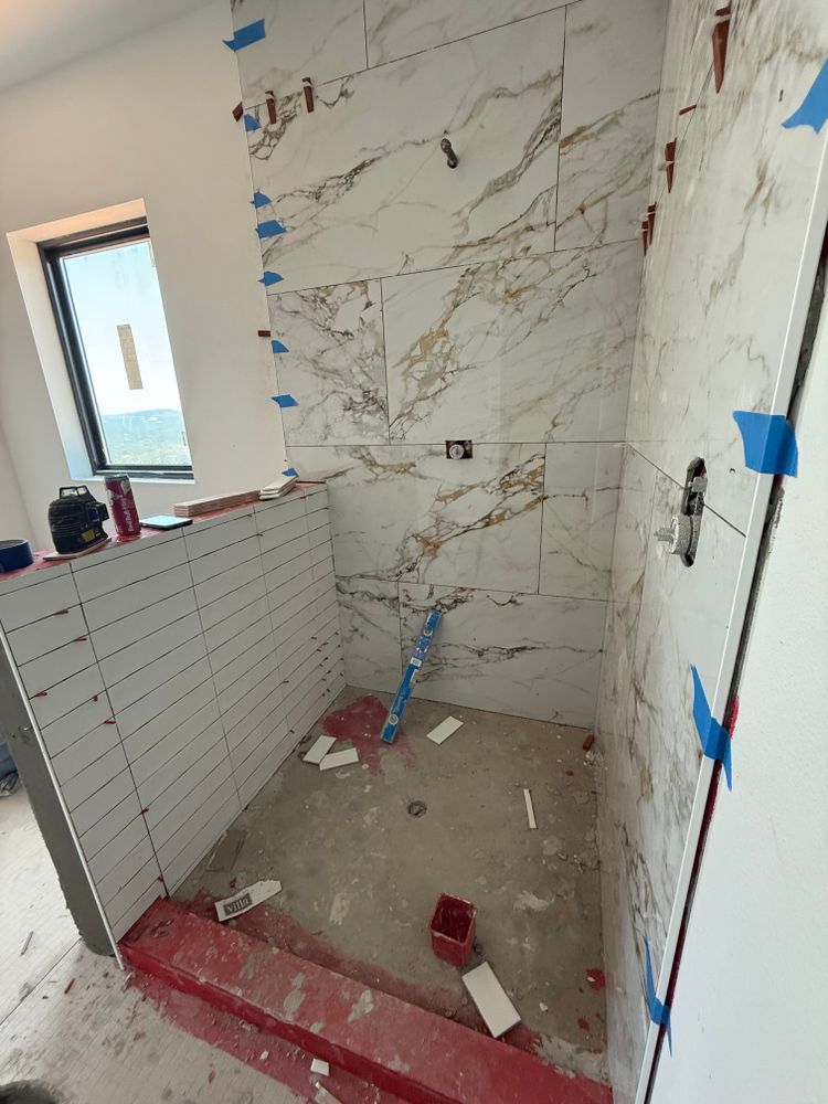 Small tiled bathroom under renovation with marble-look wall tiles, blue tape, and construction debris on the floor