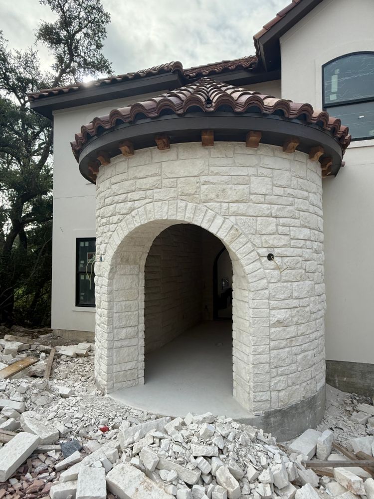 Stone arched entrance tower under construction, surrounded by rubble and unfinished stucco walls.