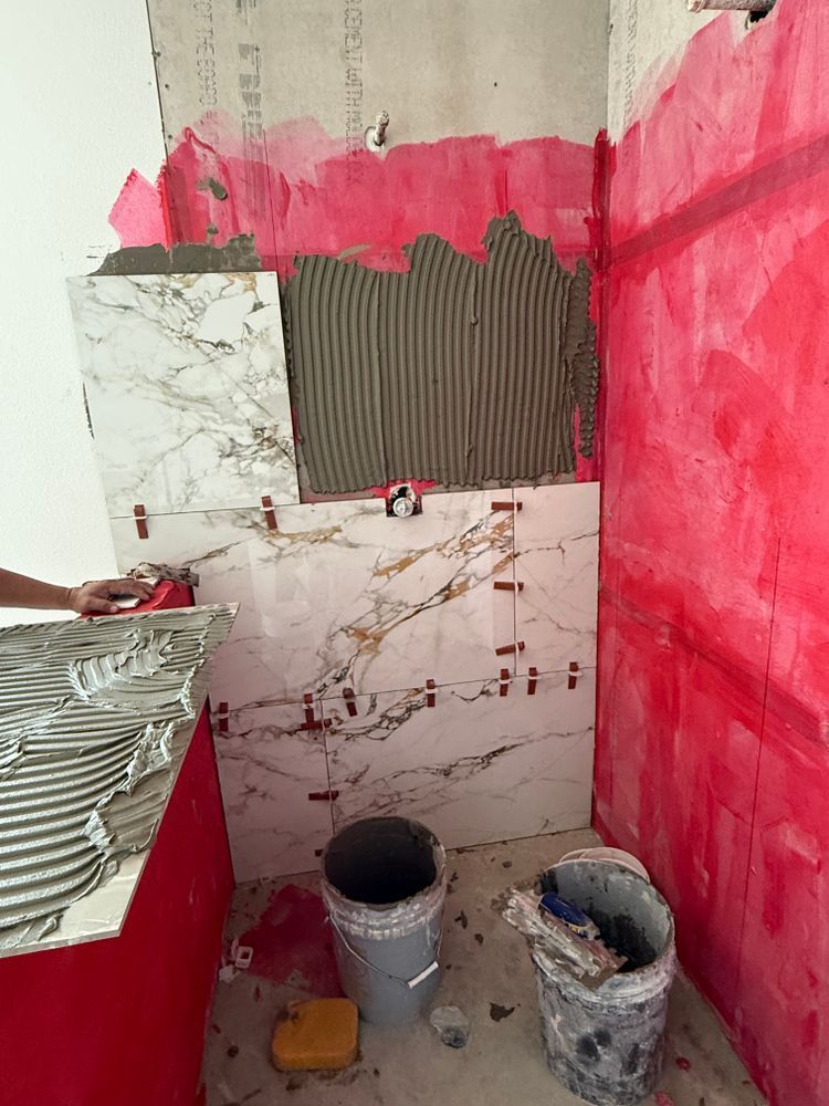 Partially tiled bathroom wall with pink paint, exposed patchwork, and paint buckets on the floor