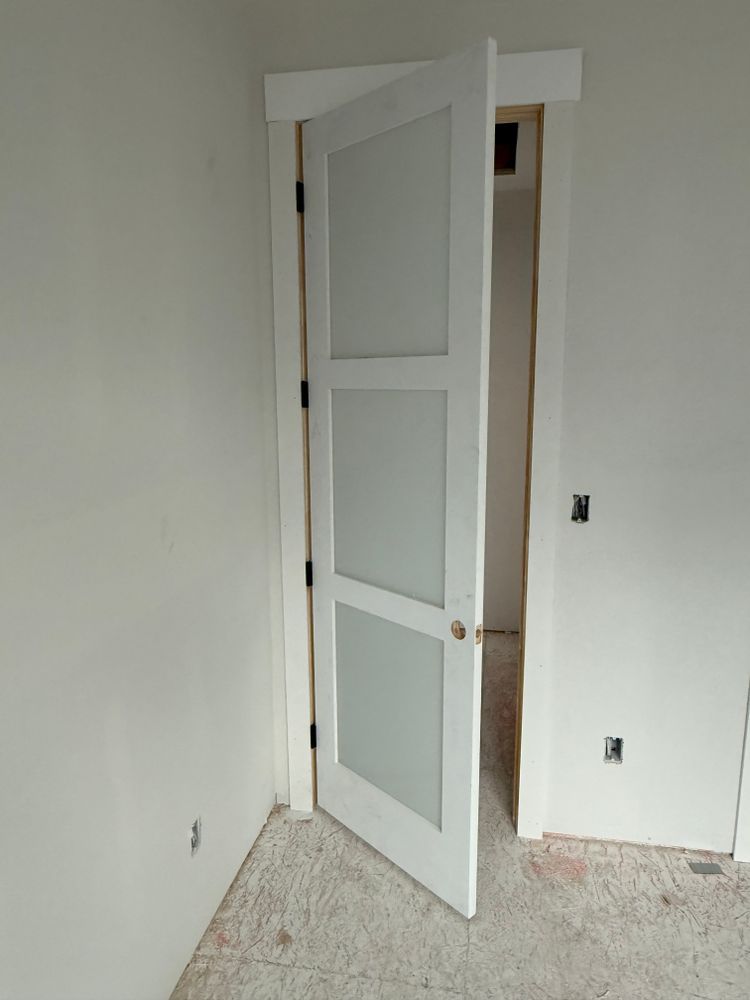Partially open white interior door in an empty room with unfinished carpet and white walls