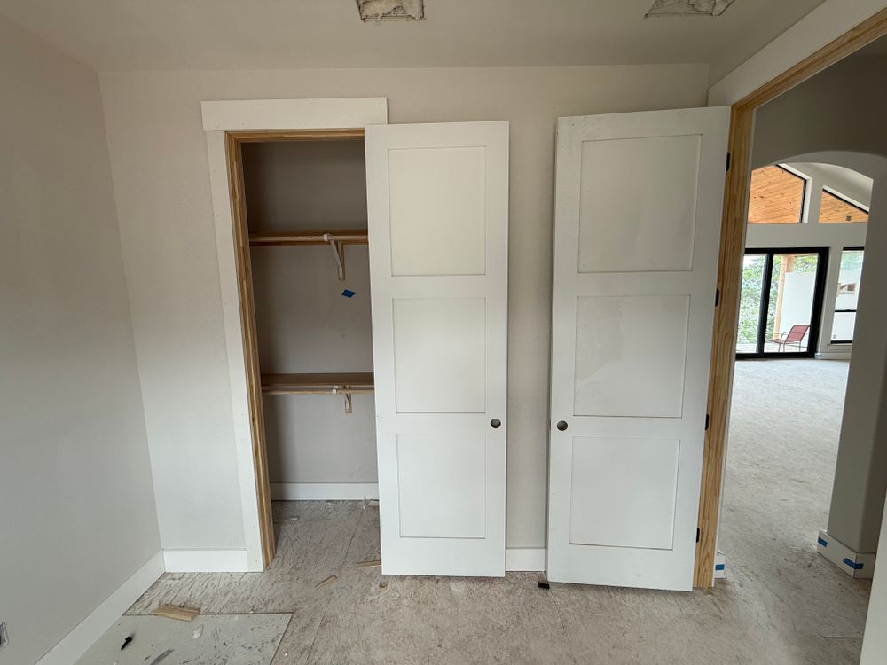 Empty room with open closet, white double doors, and arched doorway to a bright adjoining space