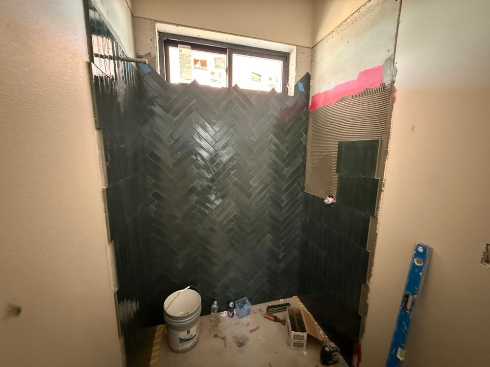 Small bathroom under renovation with black waterproof wall covering, a window, and cleaning supplies on the floor